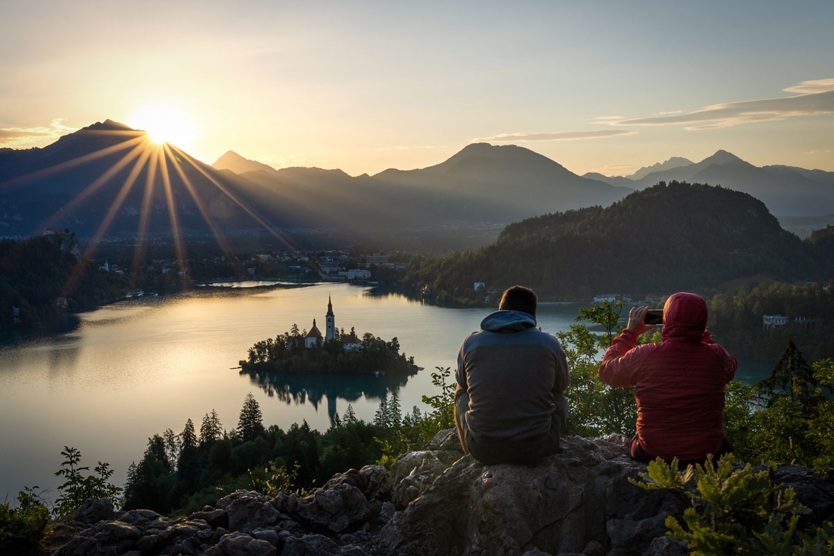 Two people watching the sunrise over Lake Bled from the hill of Ojstrica. 