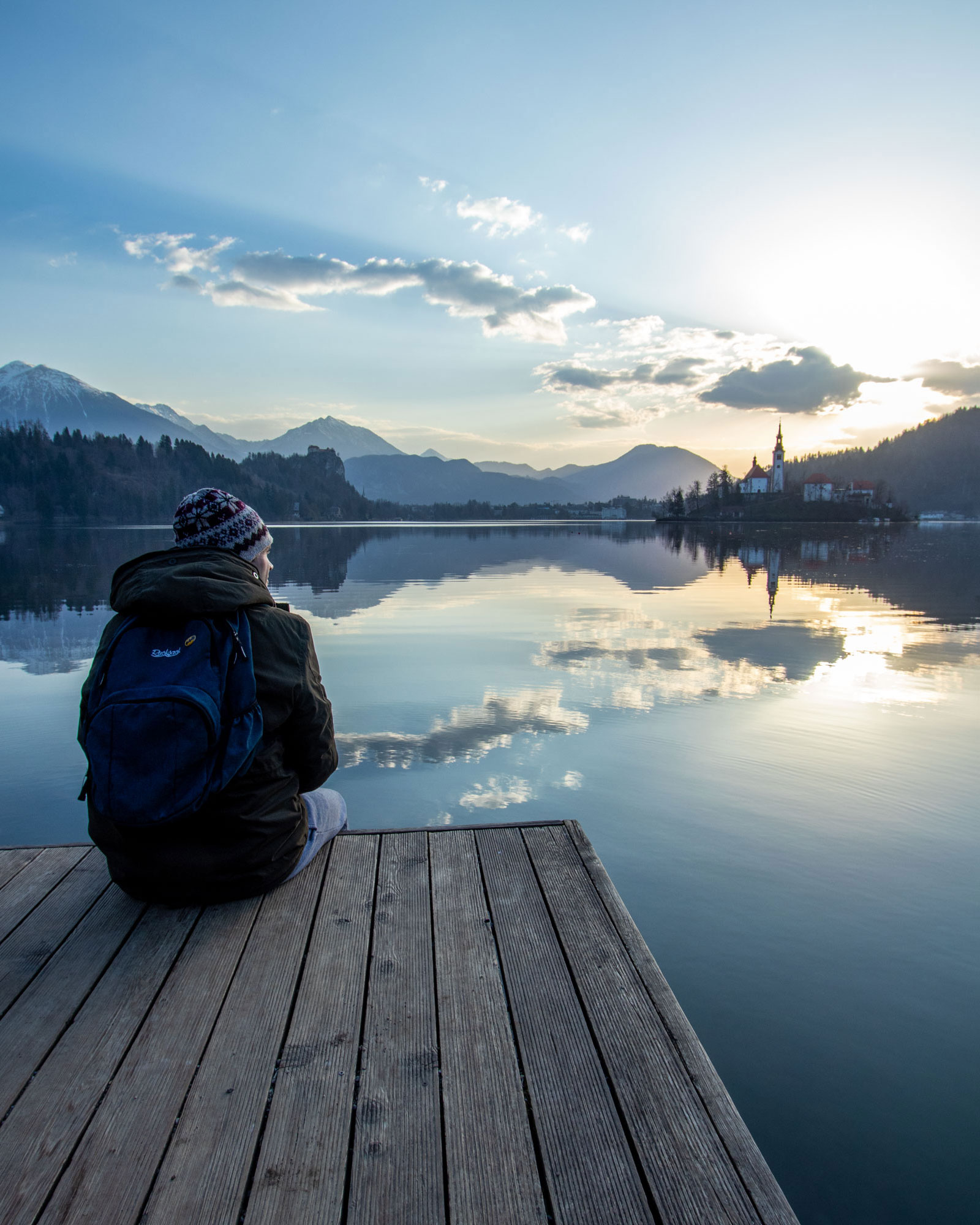 A man sits on a wooden dock at Lake Bled