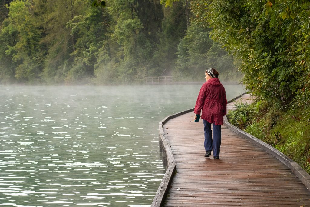 A woman walking on a wooden path above Lake Bled in autumn.